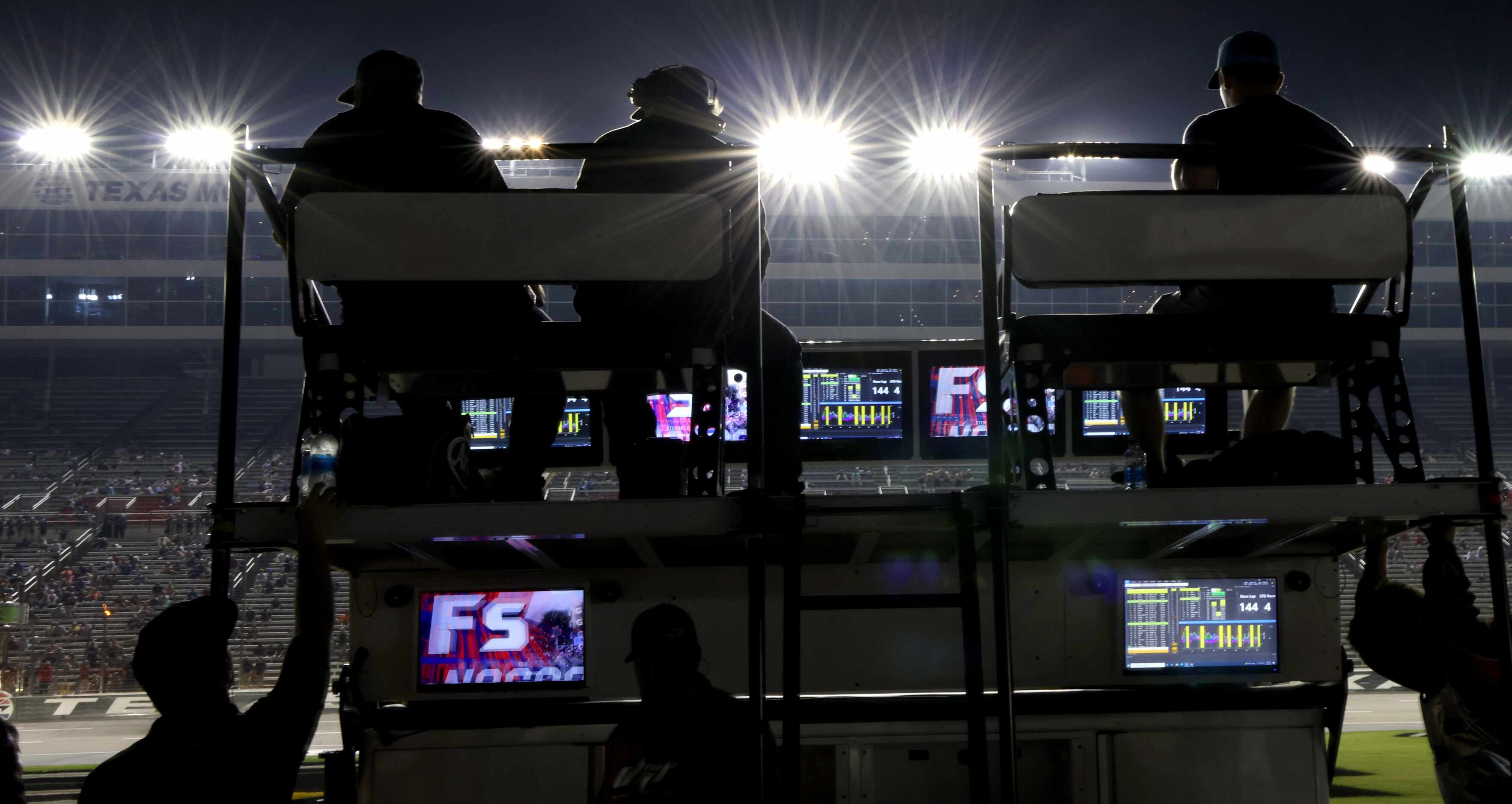 Support staff members of a racing team are silhouetted by the track lights during the final...