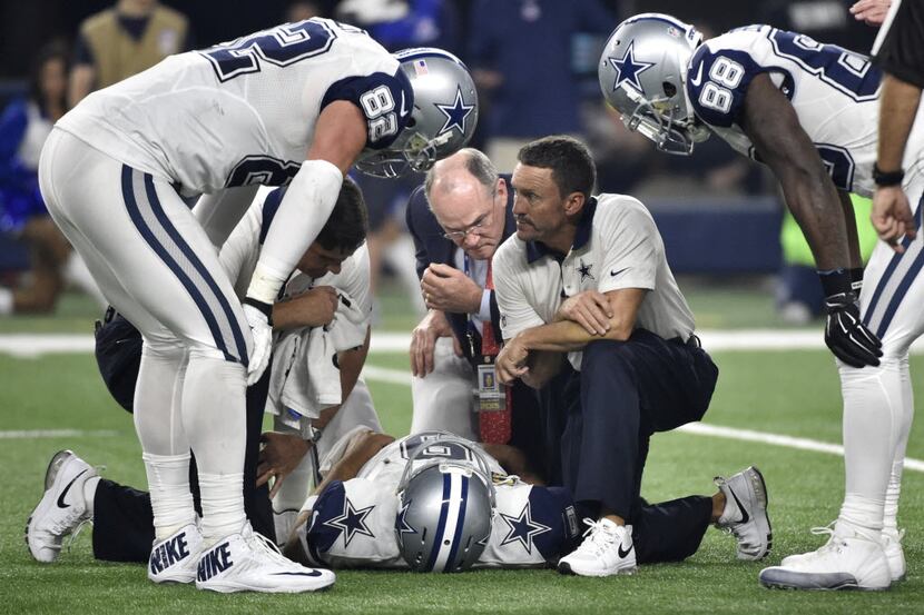 Dallas Cowboys quarterback Tony Romo lays on the ground being checked on by team staff,...