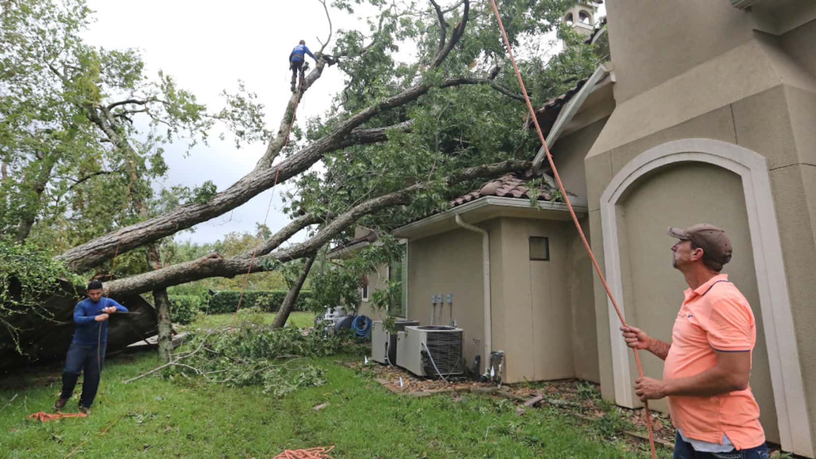 Crews work to take down trees that fell on the Odenal family residence after a tornado...