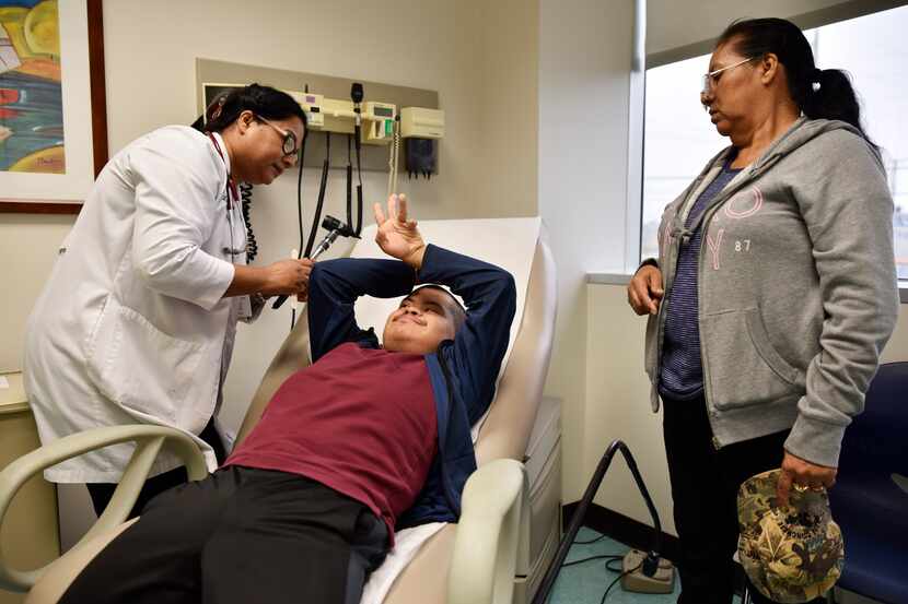 Nurse Practitioner Jhudy Mohan examines Roberto Martinez as his mother, Maria Martinez,...