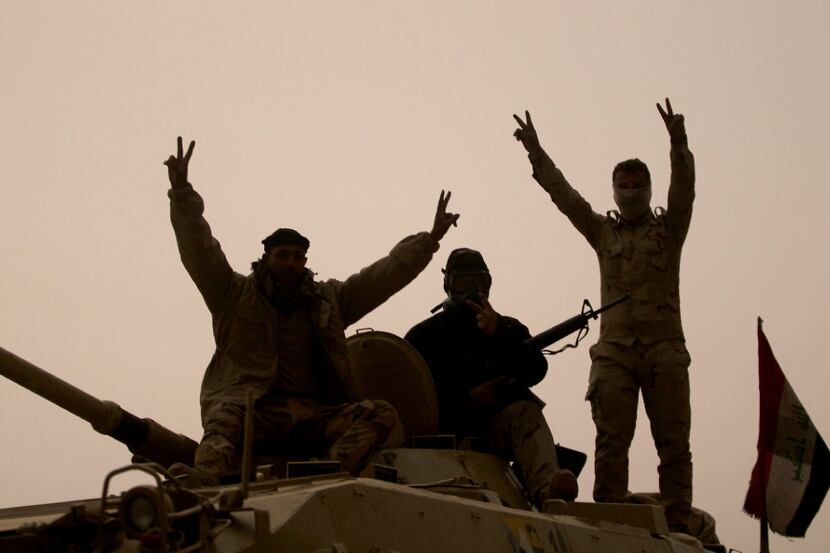 Iraqi forces flash the victory sign as they stand on an infantry fighting vehicle in the...