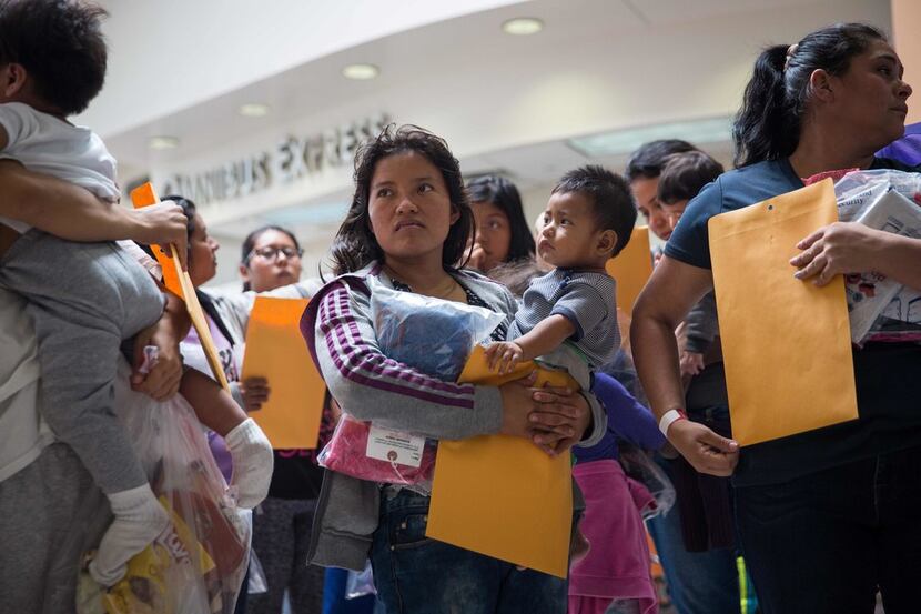 Immigrants wait to head to a nearby Catholic Charities relief center after being dropped off...