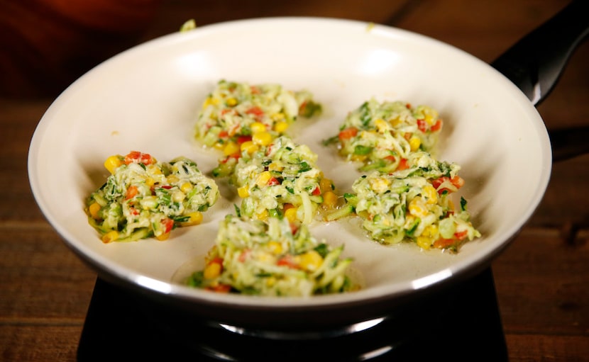 Zucchini fritters cook in a frying pan.