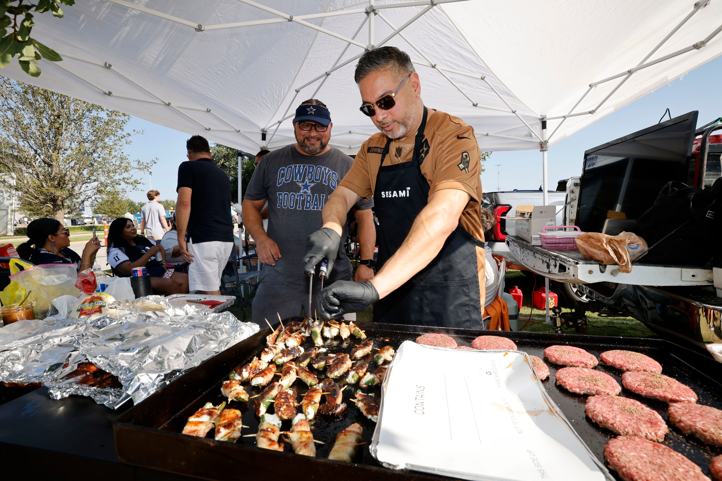 Dallas Cowboys fan James Marquez of Dallas, foreground, cooks while tailgating in the...