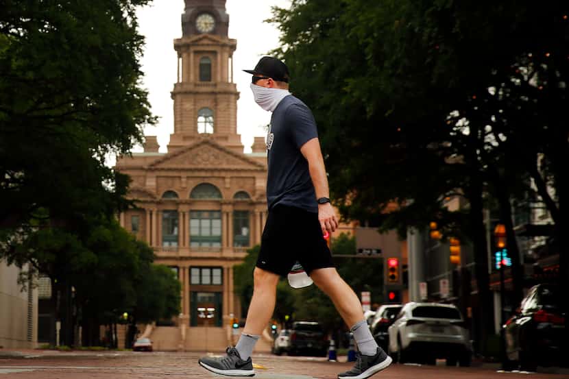 Wearing a mask, Matthew Lubinski of Bedford walks through downtown Fort Worth past the old...