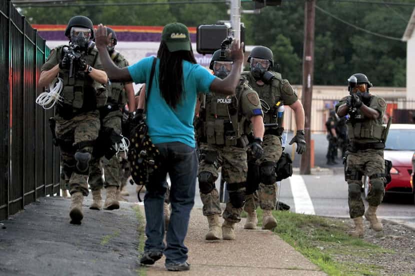 In this Aug. 11, 2014 file photo, police wearing riot gear walk toward a man with his hands...