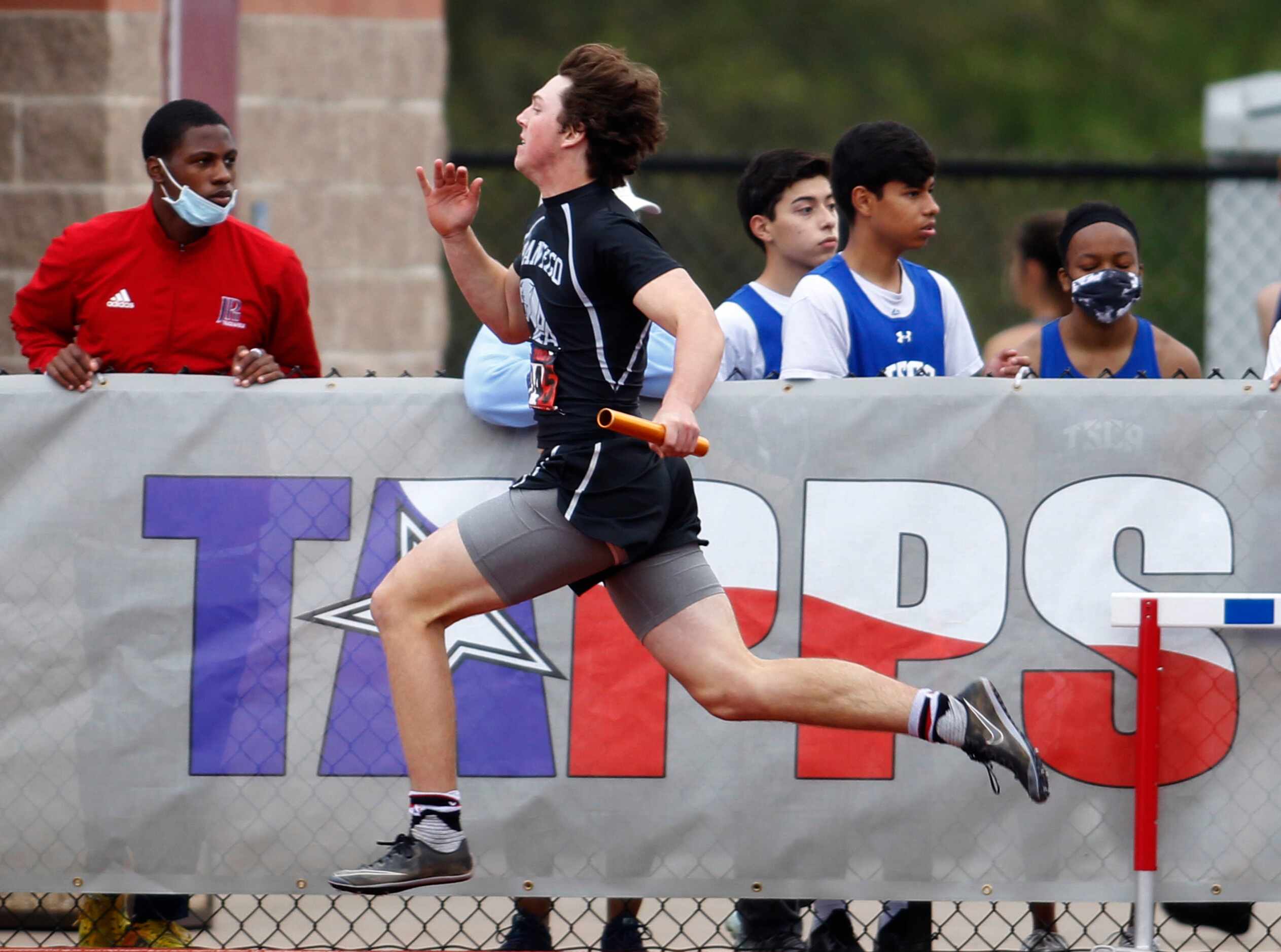 A sprinter races past a TAPPS sign during a relay event. The running finals from the TAPPS...