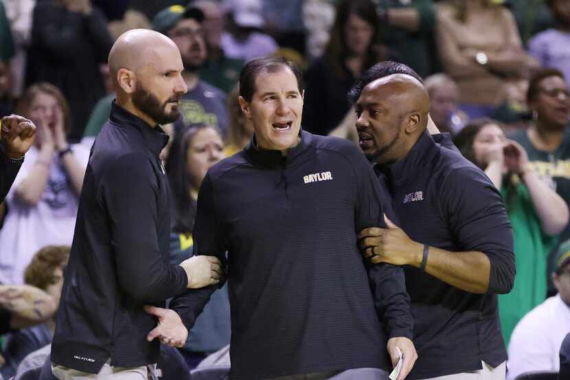FILE - Baylor head coach Scott Drew, center, is held back by assistant coaches after...