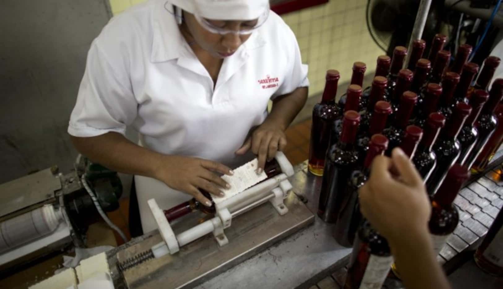 
				Trabajadores colocan etiquetes a botellas de ron Santa Teresa, en La Victoria,...
