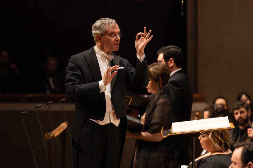 Man in a tuxedo conducts an orchestra onstage.