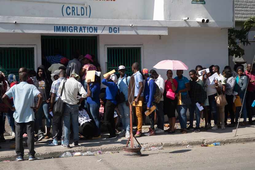 Un grupo de haitianos hacen una fila frente a una oficina de inmigración mientras esperan su...