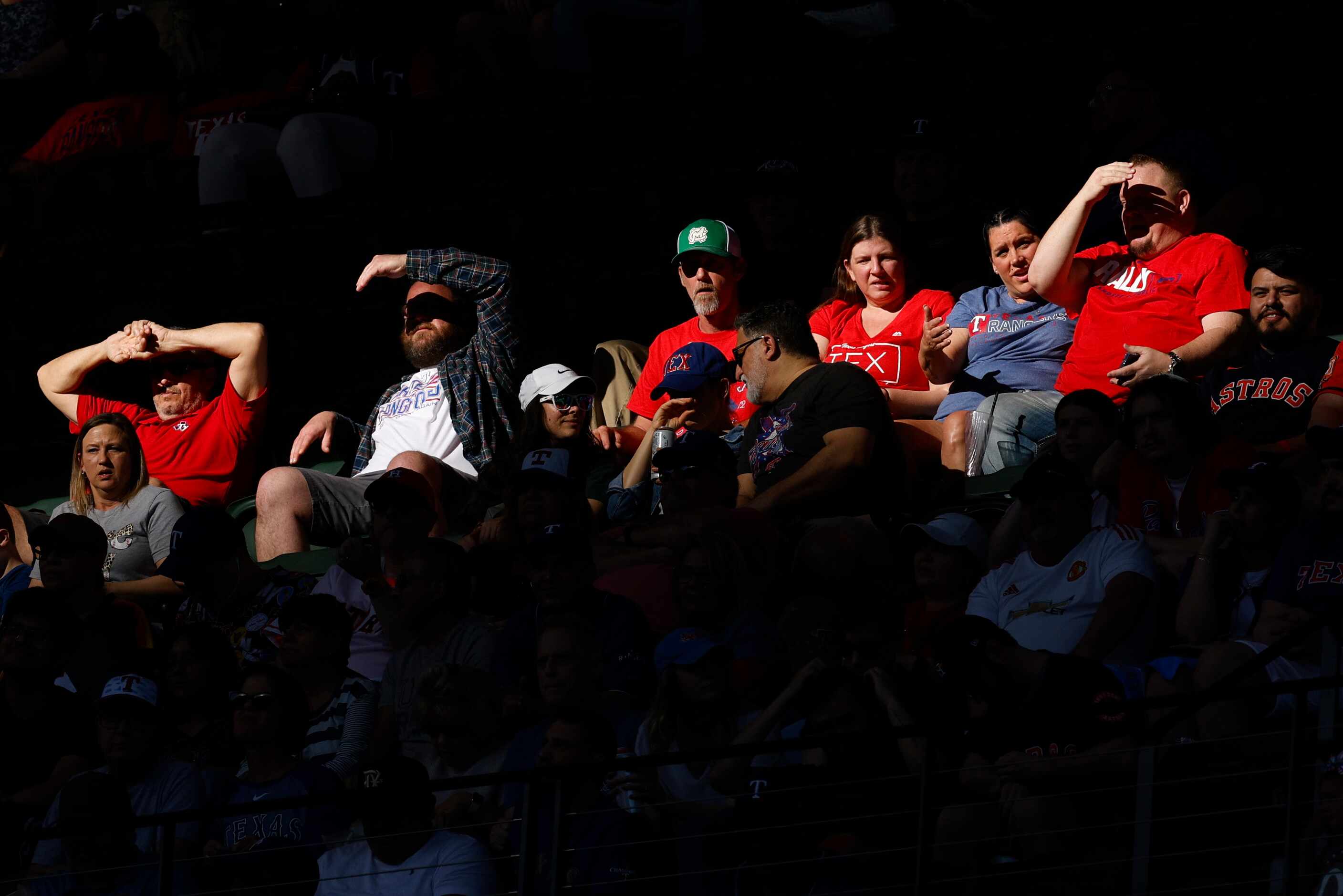 Fans shield their eyes from the sun during an MLB game between the Texas Rangers and the...