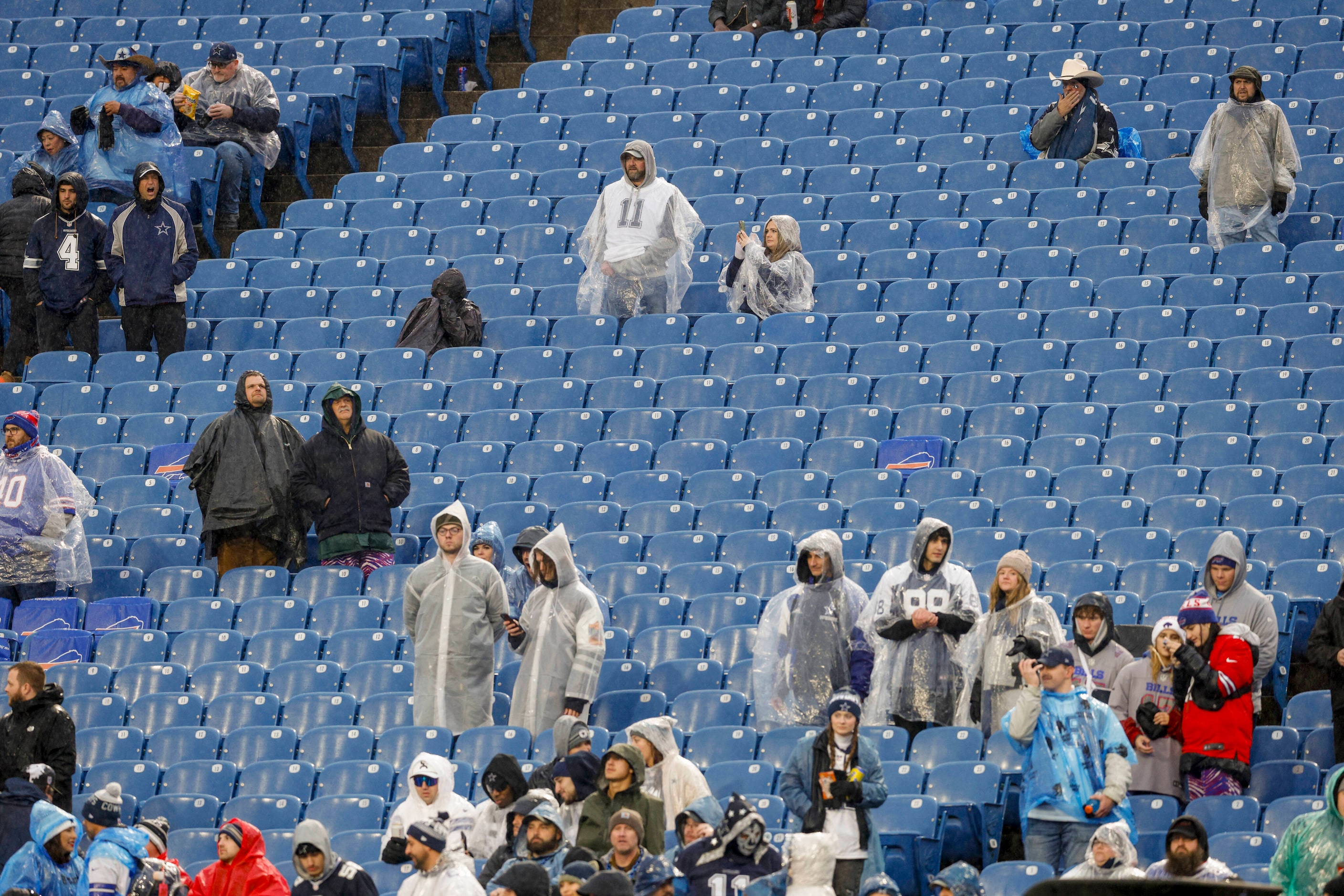 Fans use ponchos and rain jackets to shelter themselves from the elements before an NFL game...