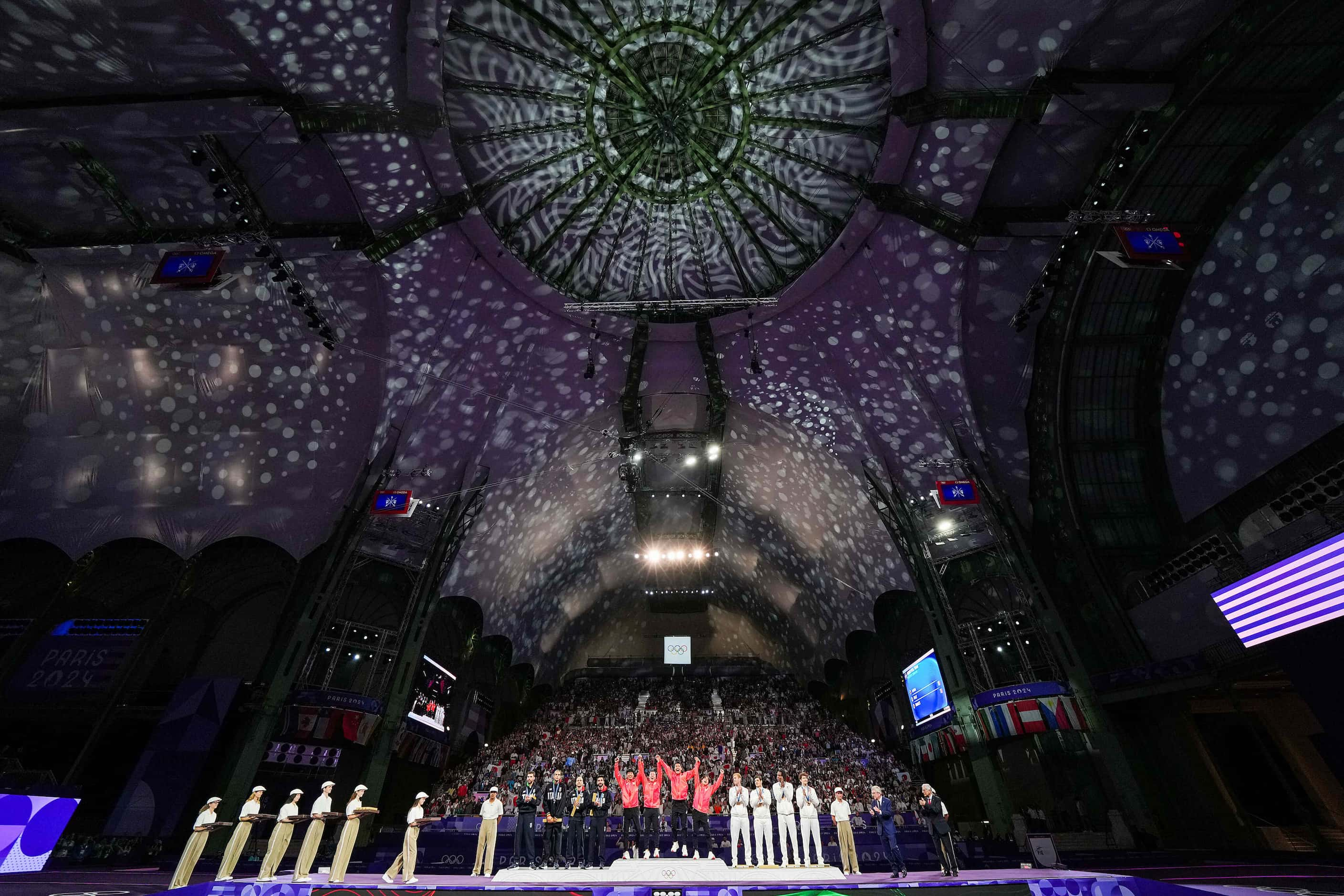 Team Japan celebrates atop the medals podium after a victory over Italy in the men’s foil...