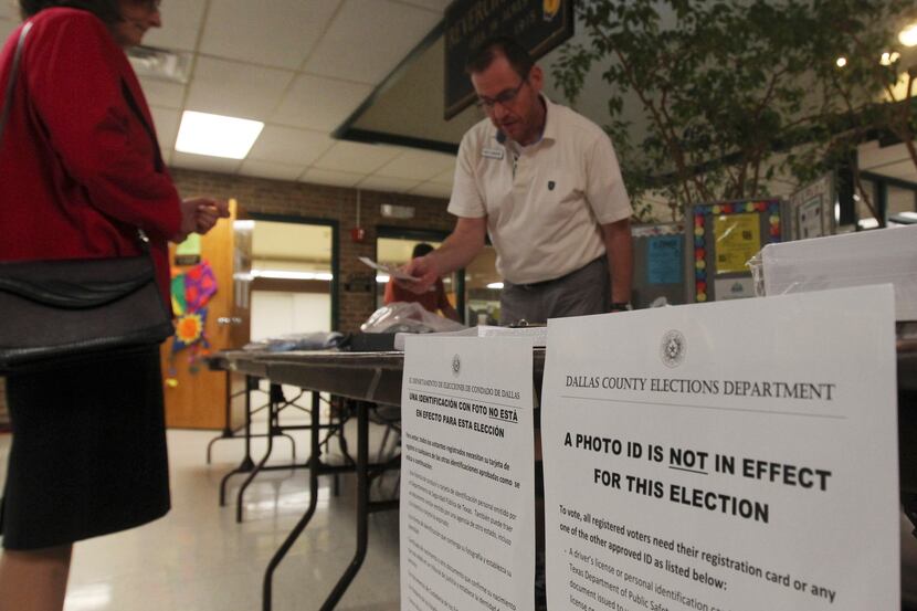 A voter waits for the polls to open as Democratic election judge Neil Emmons, right, sets up...