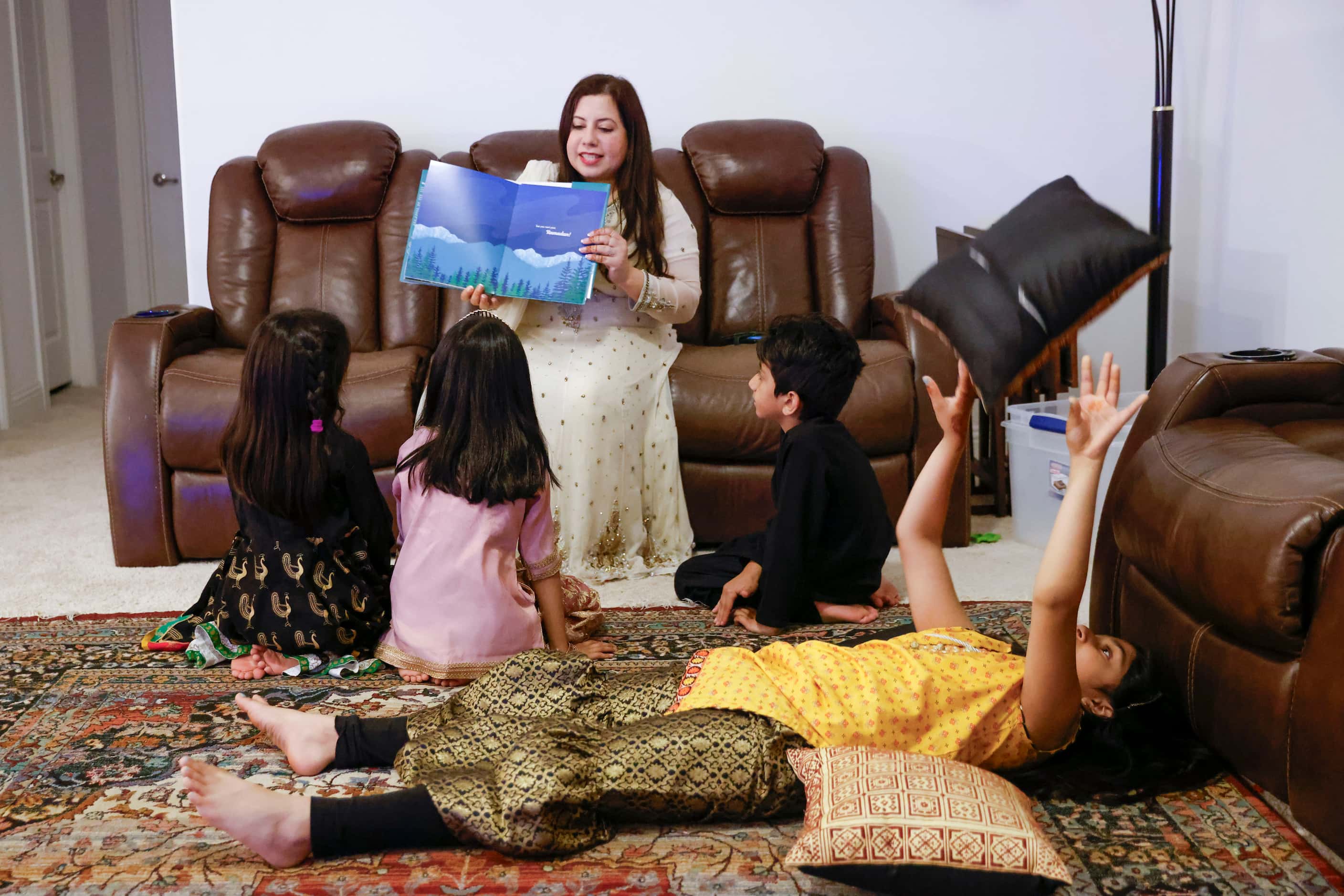 Aisha U-Kiu reads a story book as Anaya Choudhry, 8, (front), daughter of her childhood...