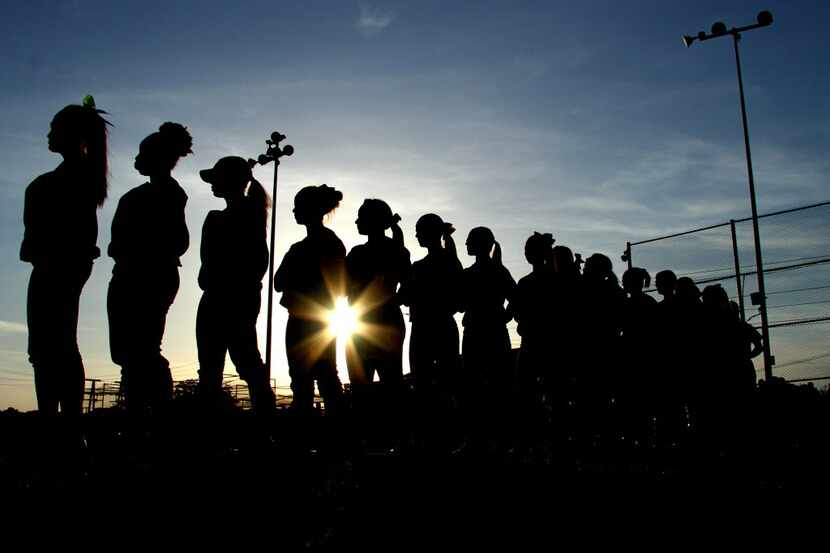 Members of the Mansfield Timberview softball team stand before a setting sun along the third...