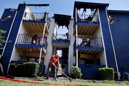 A contractor cleans up the sidewalk surrounding the burned out three-story apartment...