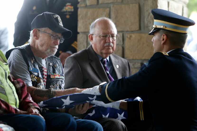 Army Capt. Gabe Stewart hands an American flag in honor of veteran Dennis Moore to Tony...