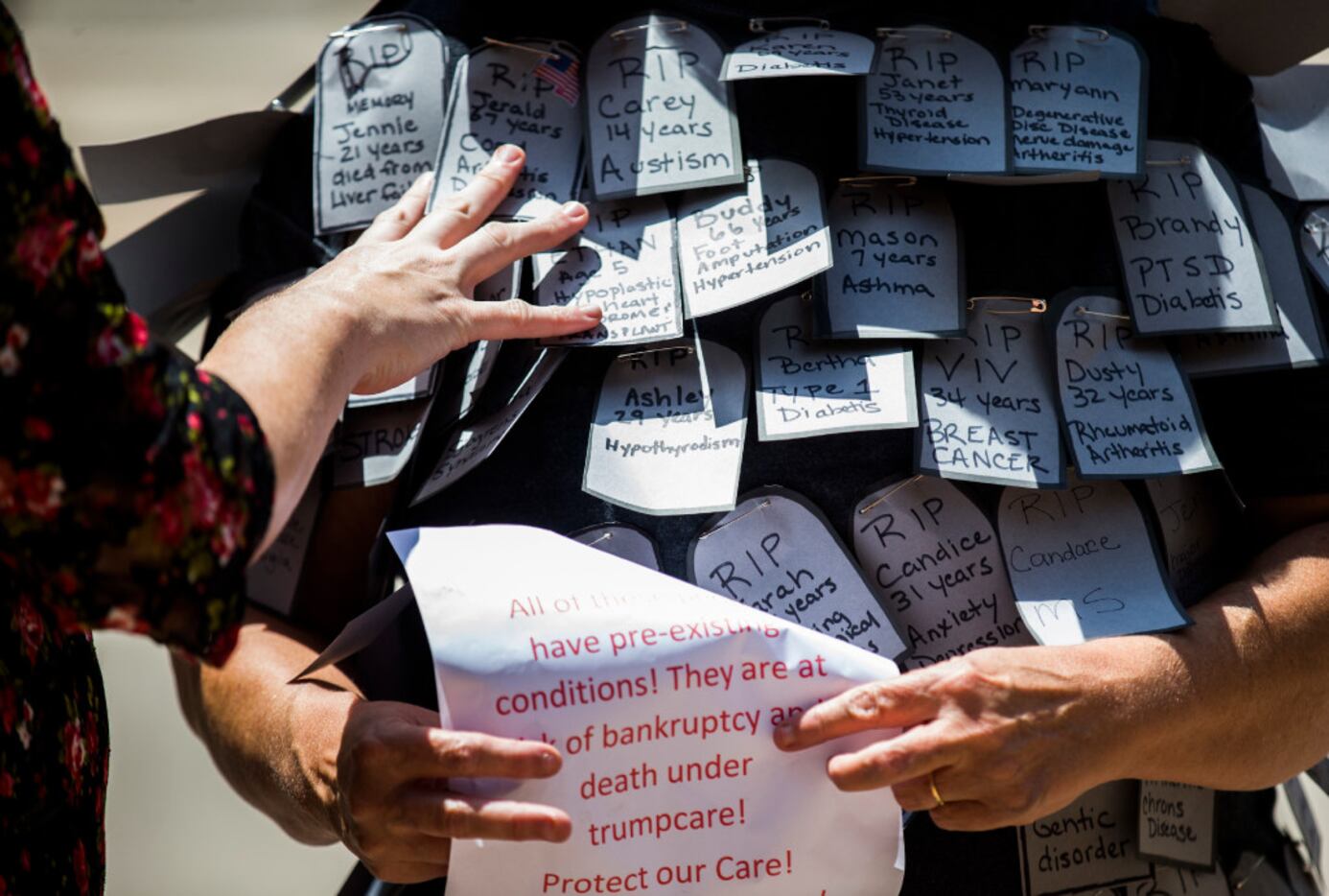 A woman sorts through paper gravestones pinned to the shirt of protester Angie Higdon of...