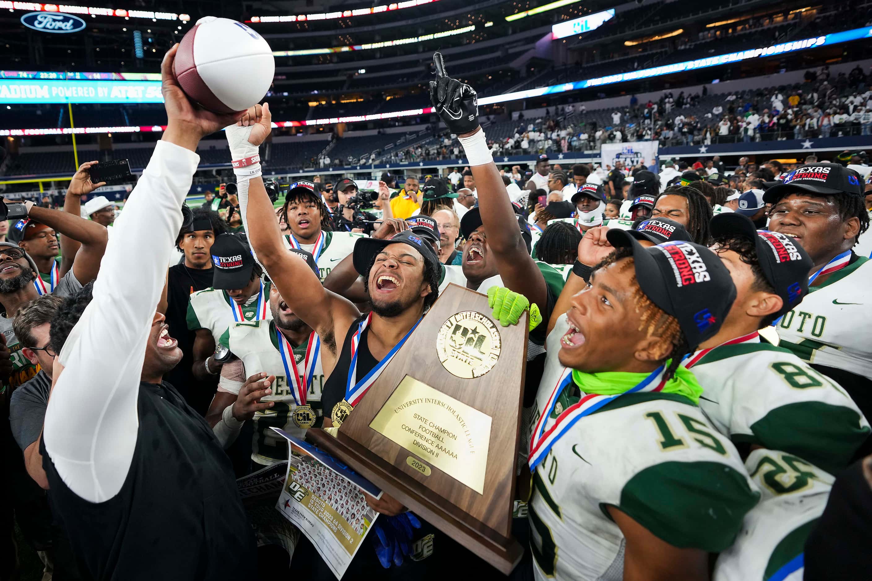 DeSoto head coach Claude Mathis lifts the game ball as players celebrate with the...