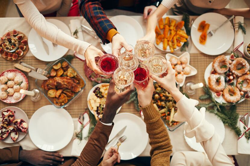People raising glasses over festive dinner table while celebrating Christmas with friends...