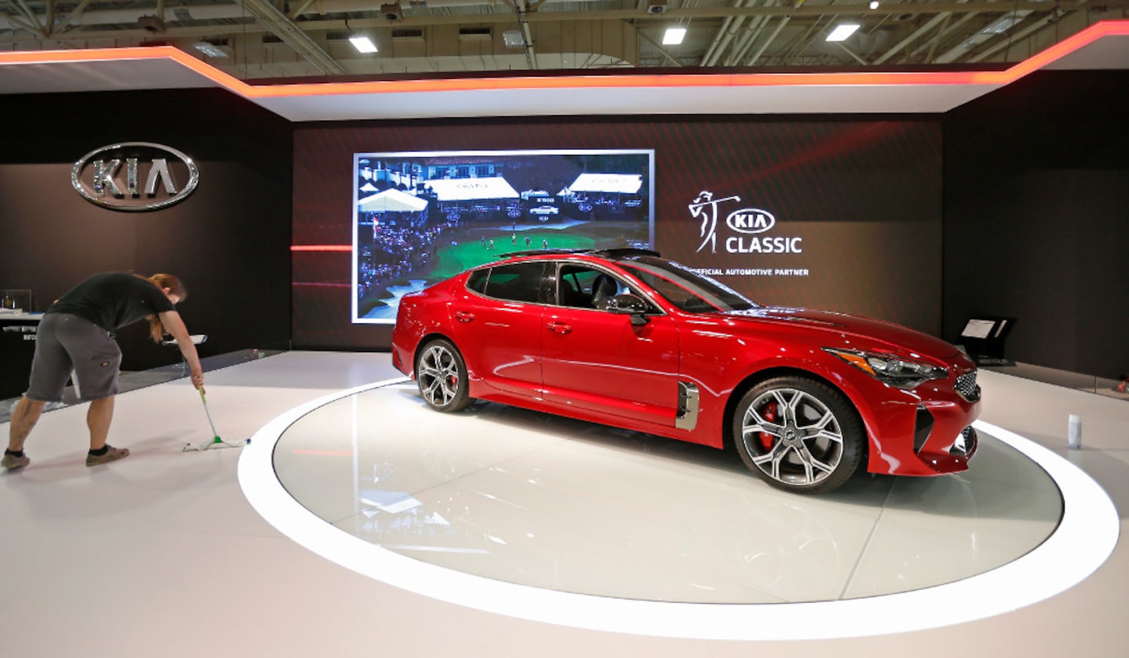 Danny Mueller sweeps the floor next to 2018 Kia Stinger, which is on display, the day before...