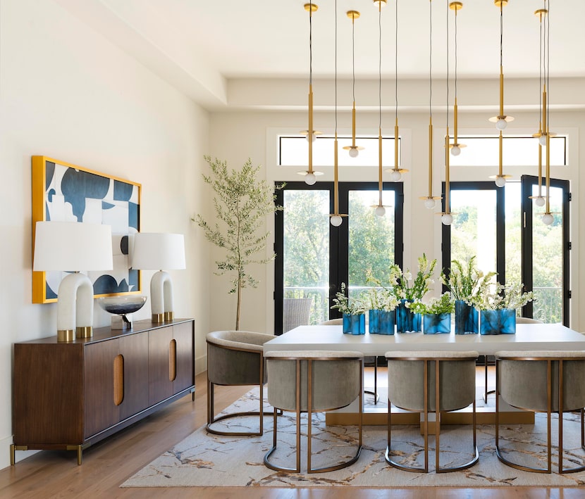 Dining room with brass light fixtures and seating around a table with blue vases and windows...