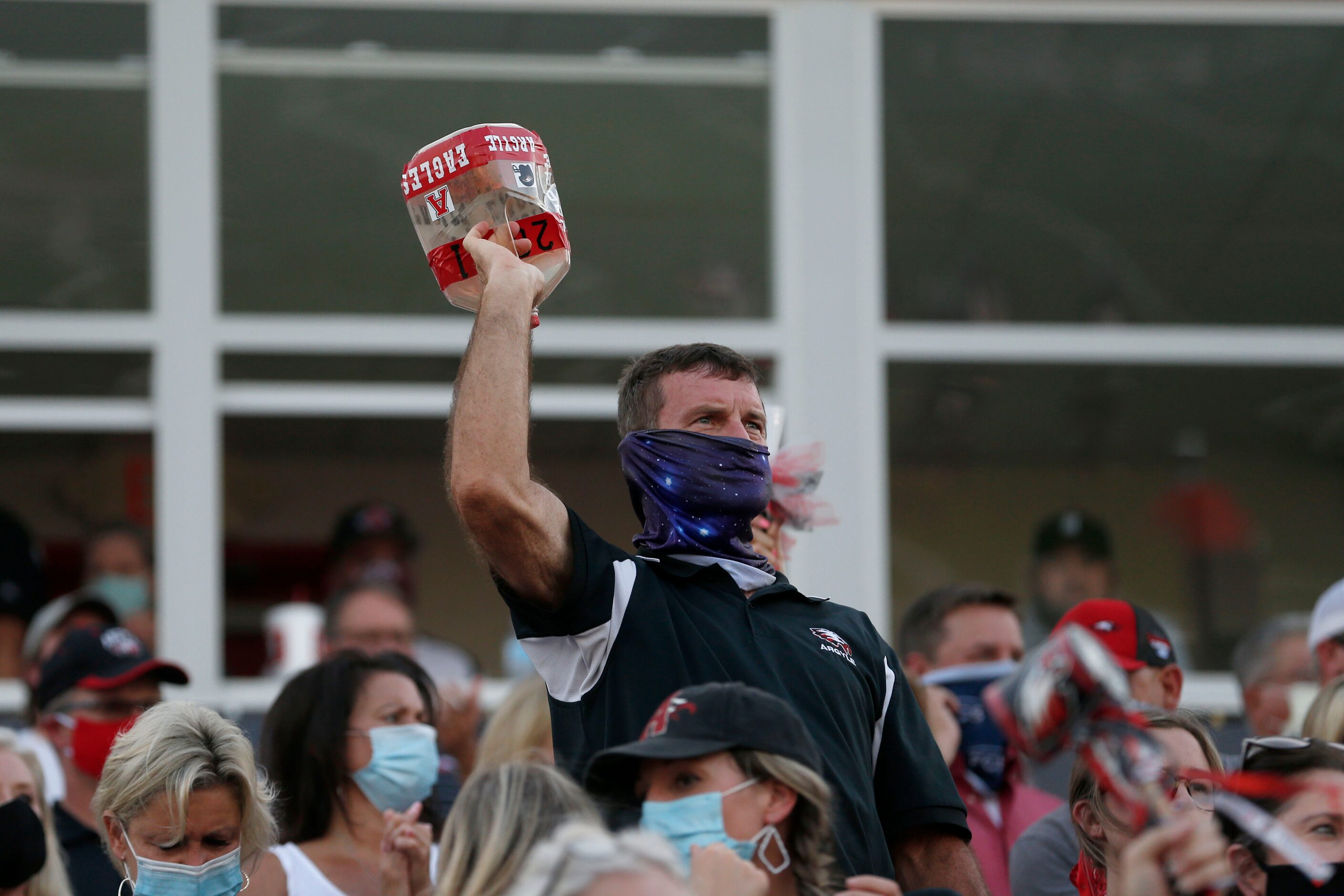 An Argyle fan wear a face covering while cheering from the stands during a high school...