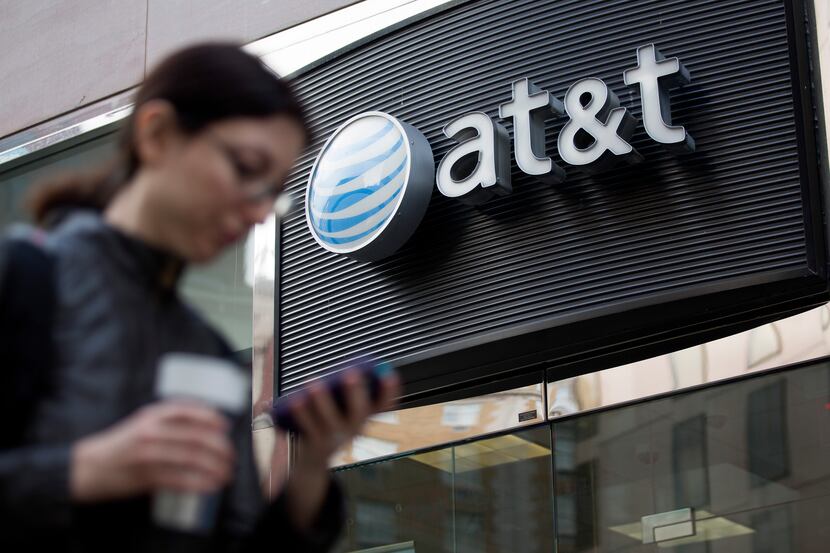 A pedestrian looks at a mobile phone while walking past an AT&T Inc. store in Washington,...