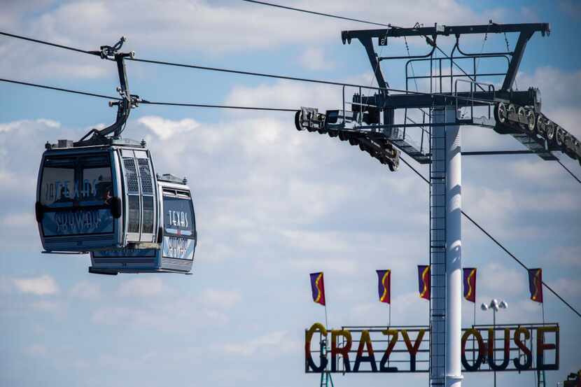 Two Texas Skyway cars pass over the Crazy House ride above the State Fair of Texas at Fair...