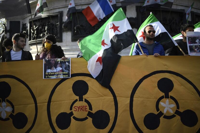 Protesters hold a banner and Syria's former independence flags (which have been adopted by...