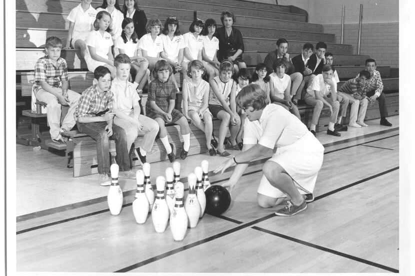 Students sitting in a gymnasium while their gym teacher teaches them how to bowl (Mar. 14,...