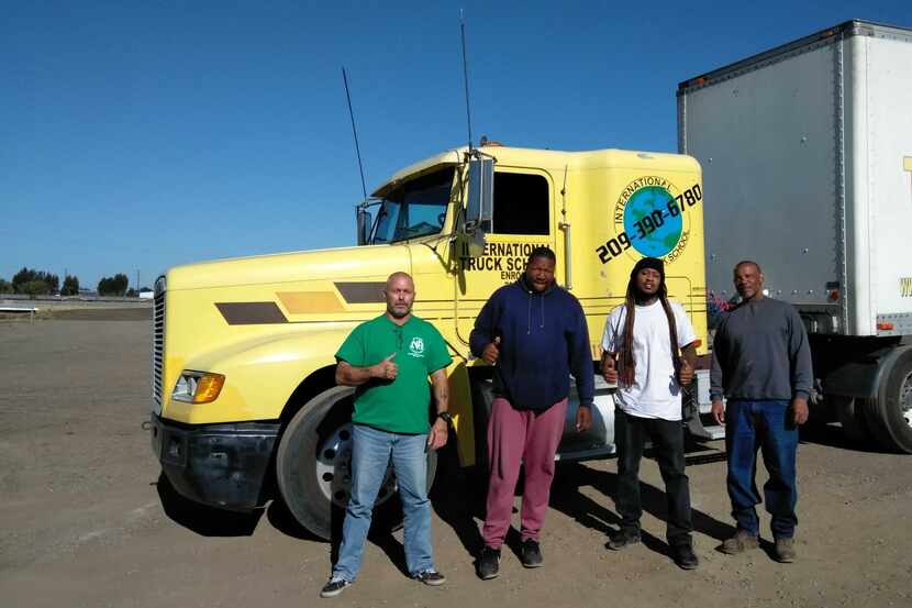 Four men stand in front of a truck after graduating to become truck drivers.