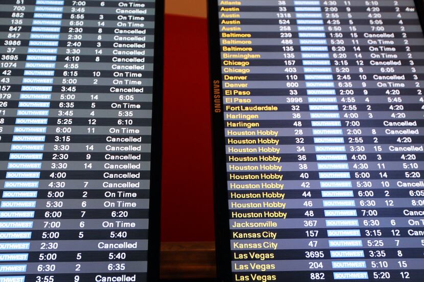 Passengers checked for cancellations and flight delays on a departure board near the...