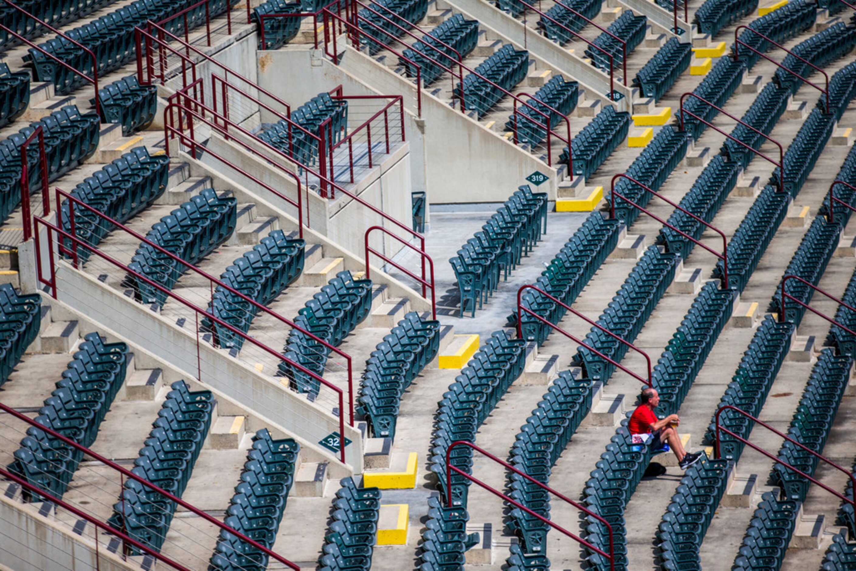 A lone Texas Rangers fan sits on the upper deck in the sun during the third inning of an MLB...