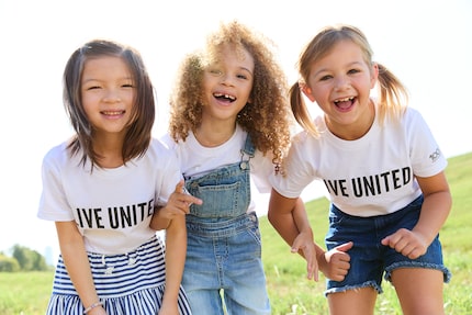 Three happy children stand together smiling while wearing t-shirts that say "Live United"