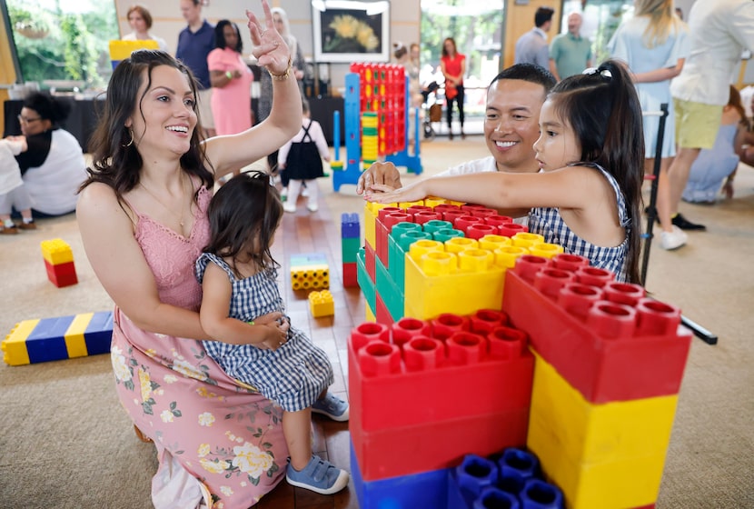 Jen Dingle waves at friends as she plays with blocks with her two children, Jia, 4 (right),...