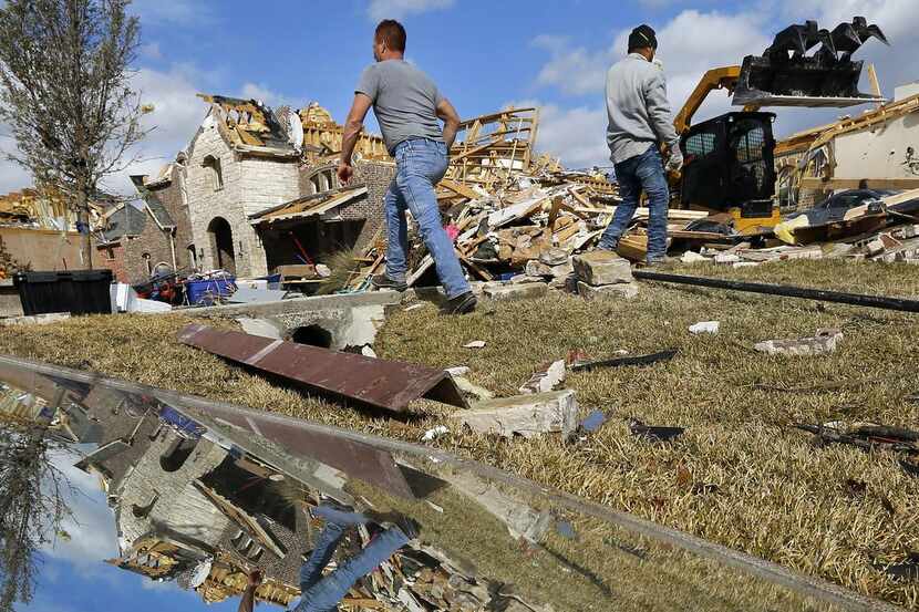 
Reflected in a salvaged mirror, Extreme Excavation workers clear tornado debris from...