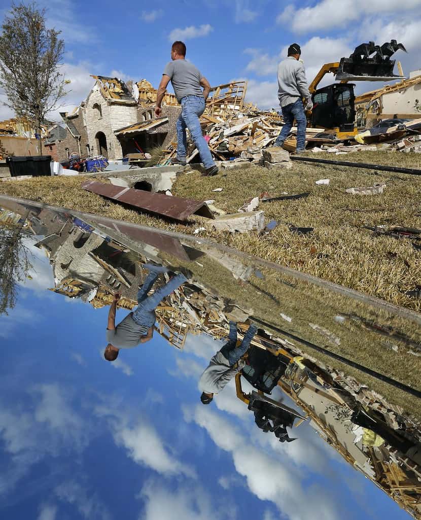 
Reflected in a salvaged mirror, Extreme Excavation workers clear tornado debris from...