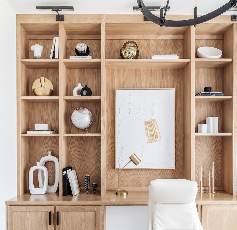 Light brown wooden bookshelves filled with small modern art pieces and hardcover books.