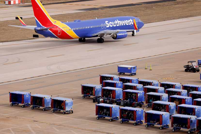 A Southwest Airlines jet passes by luggage stored in carts on the Love Field tarmac, Friday,...