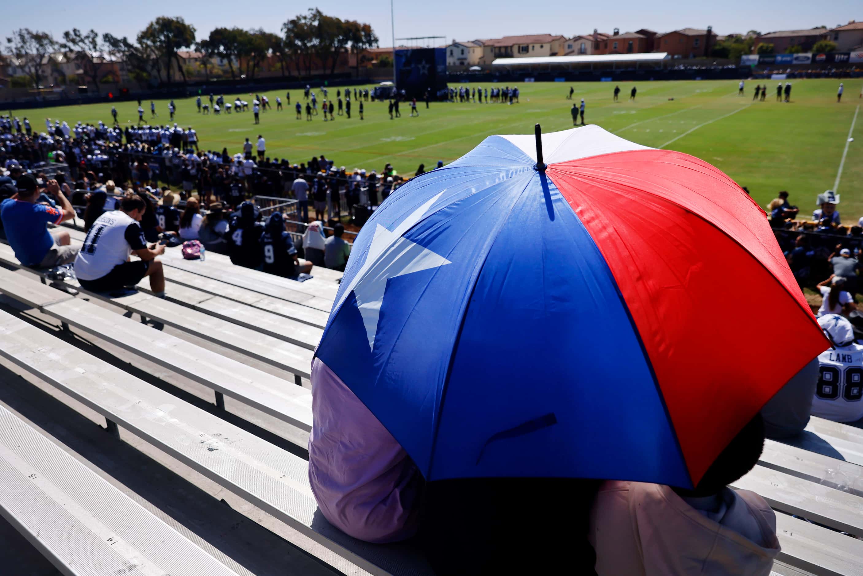 Dallas Cowboys fans take cover from the sun with a Texas flag umbrella during a training...