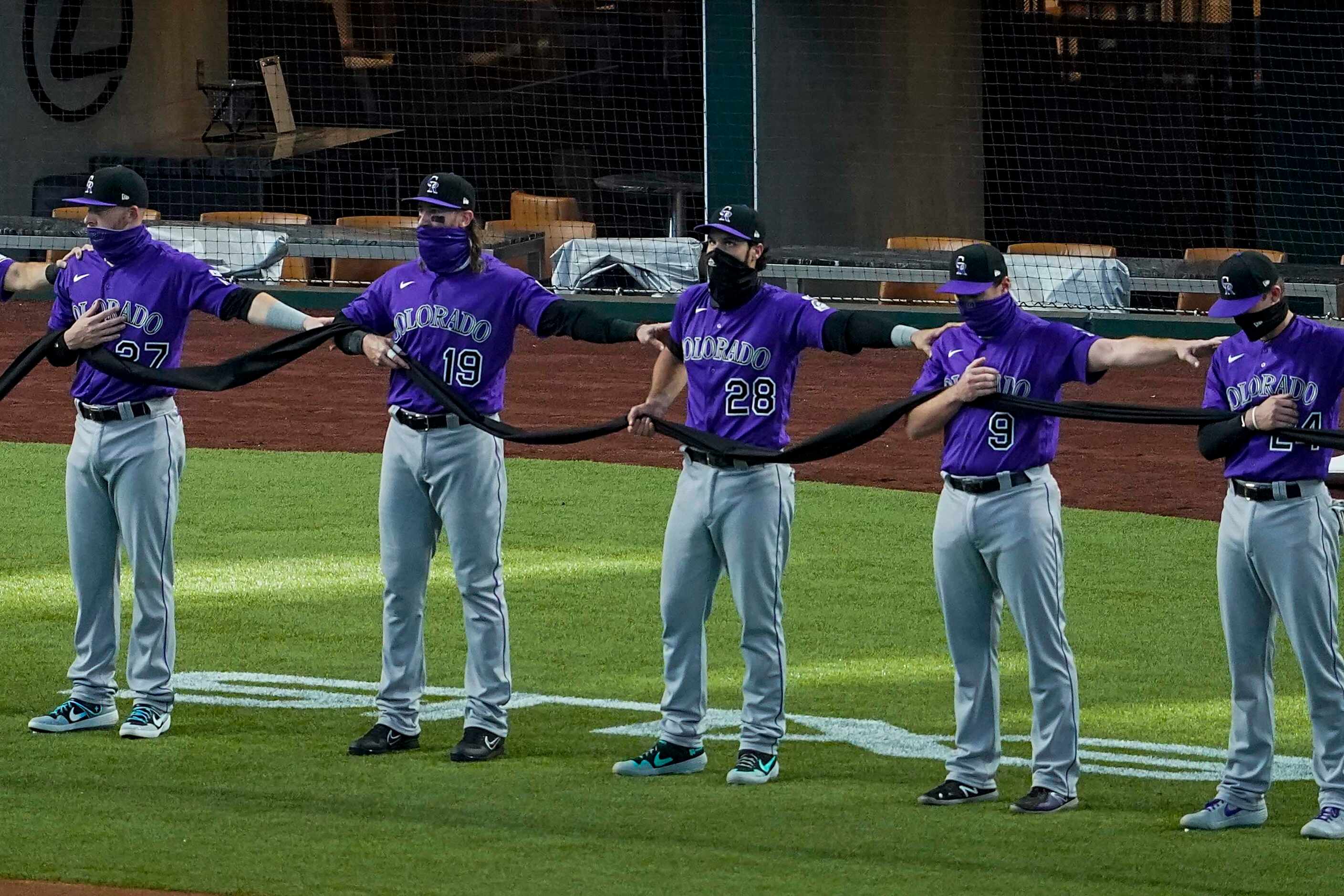 Colorado Rockies players stand arm in arm whild holding a black fabric before the singing of...