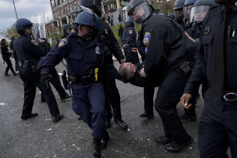 Baltimore police officers carry an injured comrade as they clash with protesters in the...