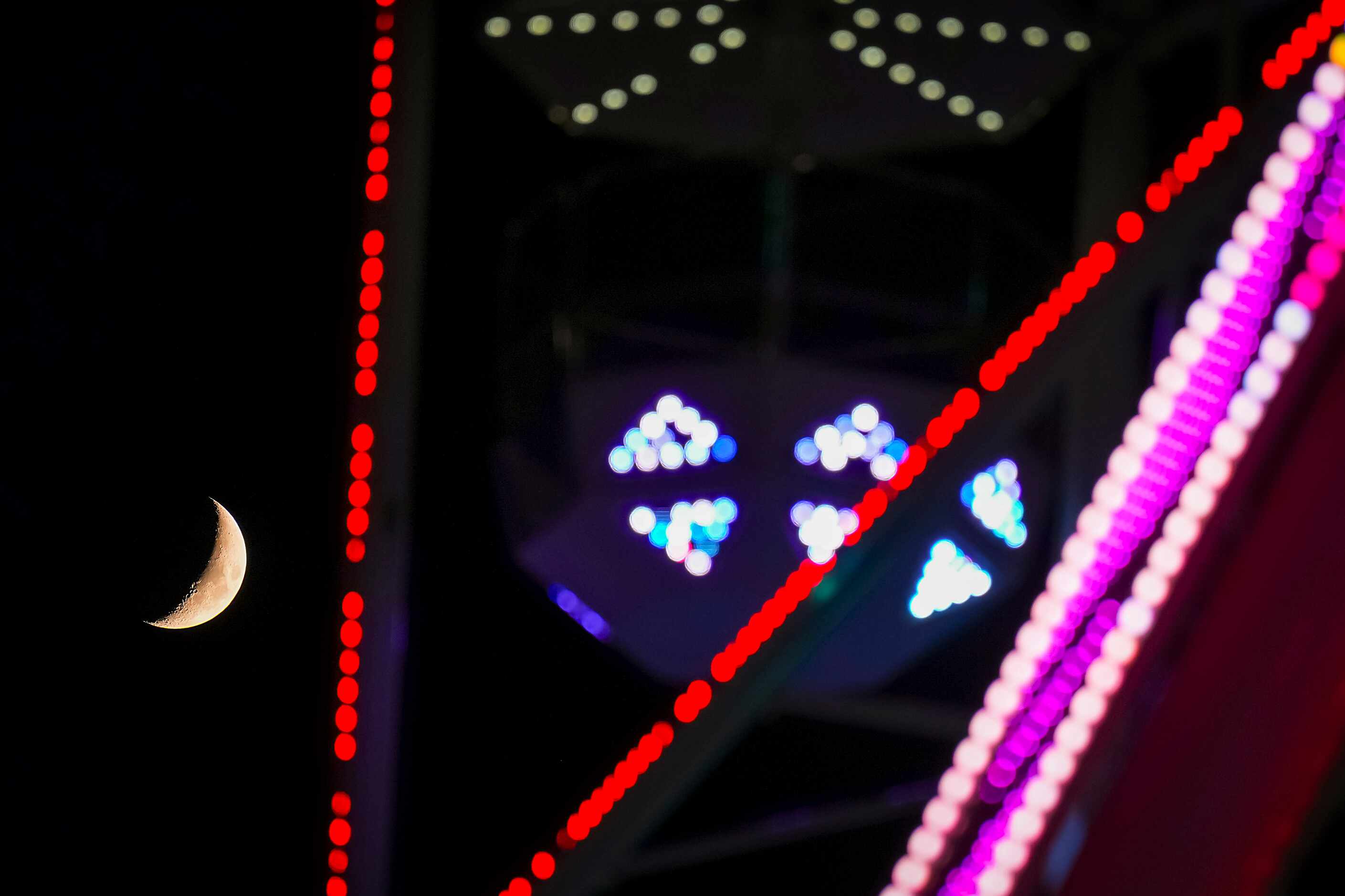 A waxing crescent moon sets behind a ferris wheel on opening day at the State Fair of Texas...