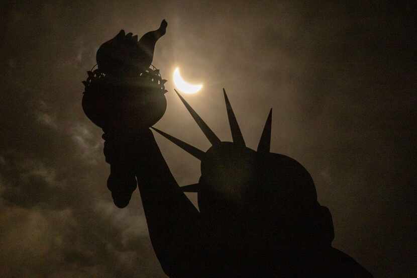 El eclipse de sol aún en etapa parcial se aprecia detrás de la Estatua de la Libertad en...
