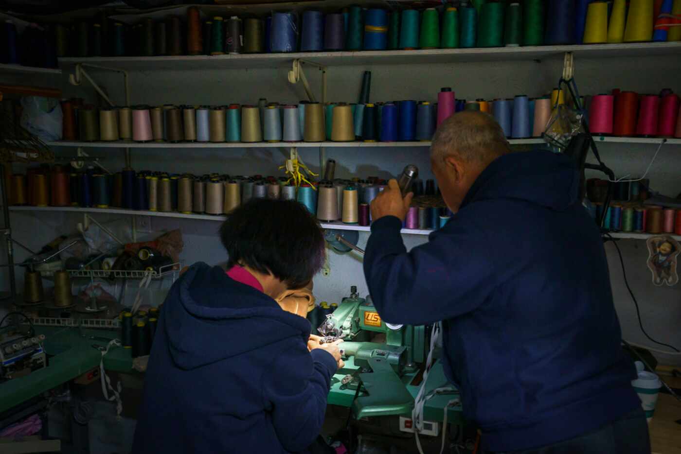 John Seok holds a flashlight for his wife Yoon Seok as she works using a sewing machine at...