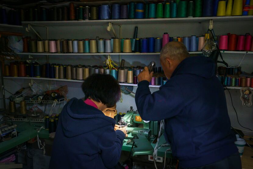 John Seok held a flashlight for his wife, Yoon Seok, as she worked using a sewing machine at...