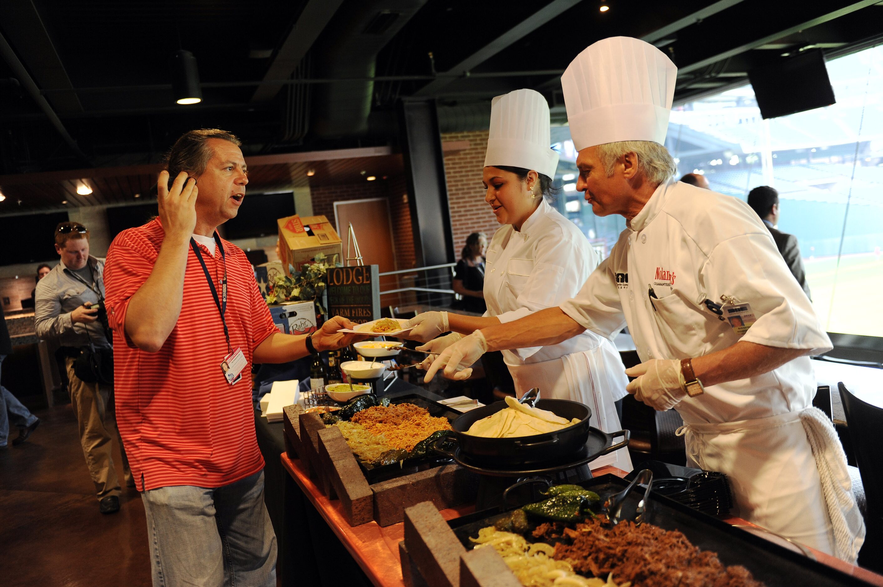 Ted Nichols-Payne (left) is served some food inside the Batter's Eye Club at Rangers...